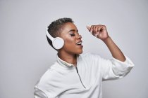 Mulher étnica energética em fones de ouvido sem fio e roupas da moda dançando hip hop com boca aberta e olhos fechados — Fotografia de Stock