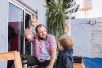Barbuto allegro papà insegnamento figlio con martello lavorare con legno mentre seduto sul lungomare nel fine settimana — Foto stock