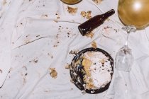 Dall'alto torta fracassata per celebrazione di compleanno su panno disordinato sbriciolato vicino a palloncini il bicchiere da vino e le bottiglie a partito — Foto stock