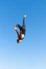 Visão lateral de baixo ângulo do atleta masculino ativo fazendo backbend enquanto salta contra palmeiras sob o céu azul sob a luz solar — Fotografia de Stock