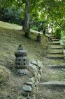 Linterna asiática de piedra rugosa sobre terreno contra escalera y arbustos en parque de Bali Indonesia - foto de stock