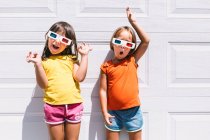 Allegro ragazze carine in abiti colorati casual e occhiali tridimensionali in piedi su sfondo bianco parete — Foto stock