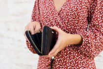 Ernte unkenntliche Frau in rotem Kleid steht und öffnet schwarze Ledertasche gegen helle Wand am Tag — Stockfoto