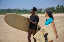 Sportive noire souriante avec longboard contre petite amie asiatique avec planche de surf regardant vers l'avant dans l'océan sous un ciel bleu nuageux — Photo de stock