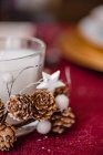 Candle in glass holder decorated with cones and stars placed on table served for celebrating Christmas — Stock Photo