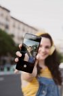 Mujer despreocupada en auriculares inalámbricos tomando selfie en el teléfono celular en la calle - foto de stock