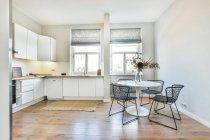 Просторная светлая кухня с белыми шкафами и обеденной зоной с белым столом и стульями у окна — стоковое фото