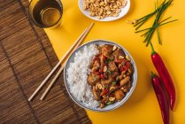 Oberseite der Komposition Schüssel mit Kung-Pao-Huhn mit weißem Reis Erdnuss und roter Chilischote und grünen Zwiebeln und Essstäbchen — Stockfoto