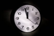 Круглий мінімалістичний годинник з цифрами та стрілками на чорному тлі — стокове фото