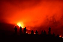 Human silhouettes standing recording and photographing with tripods the lava explosion in La Palma Canary Islands 2021 and several unfocused silhouettes seated observing the natural phenomenon. — Stock Photo