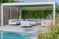 Jarda de mansão moderna cara com piscina e zona de estar com sofás confortáveis e poltronas sob o céu azul — Fotografia de Stock