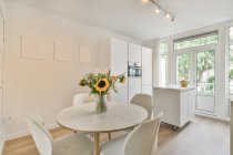 Mesa redonda com buquê de flores colocadas perto da cozinha leve no apartamento moderno durante o dia — Fotografia de Stock