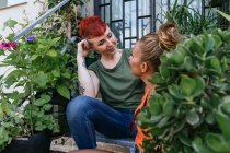 Content young tattooed woman speaking with homosexual beloved while looking at each other on staircase between plants — Stock Photo