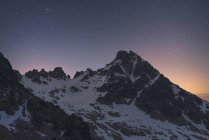 Сценический вид темных гор со снегом и грубыми вершинами под звездным небом в сумерках — стоковое фото