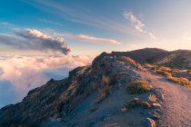 Sunrise on a high altitude mountain trail amid soft, thick white clouds and the eruption of a volcano in the background. Cumbre Vieja volcanic eruption in La Palma Canary Islands, Spain, 2021 — Stock Photo
