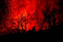 Человеческий силуэт, сидящий против взрывающейся лавы и магмы, вытекающей из кратера. Извержение вулкана Кумбре-Вьеха на Канарских островах, Испания, 2021 г. — стоковое фото