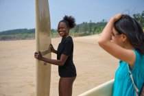 Sportive noire souriante avec longboard contre petite amie asiatique avec planche de surf regardant vers l'avant dans l'océan sous un ciel bleu nuageux — Photo de stock