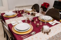Сверху сервировка стола со стаканами и столовыми приборами рядом с тарелками, украшенными свечами и конусами для празднования Рождества — стоковое фото