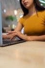 Cultivado joven emprendedora irreconocible sentado a la mesa y navegar netbook mientras se trabaja en el lugar de trabajo moderno - foto de stock