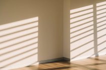 Intérieur du couloir loft spacieux vide avec des ombres géométriques et la lumière du soleil sur les murs blancs — Photo de stock