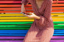 Crop unrecognizable female in dress sitting on colorful bench and browsing mobile phone in daytime — Stock Photo