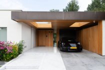 Moderner Sportwagen parkt im Hinterhof einer stilvollen minimalistischen Villa, die an sonnigen Tagen mit blühenden Pflanzen dekoriert ist — Stockfoto