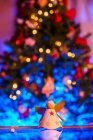 Brinquedo feito à mão em forma de anjo colocado na mesa de reflexão contra a árvore de Natal festiva com guirlandas brilhantes — Fotografia de Stock
