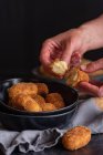 Crop persona irriconoscibile dimostrando la metà di crocchette fritte gustose con ripieno di formaggio su sfondo nero — Foto stock