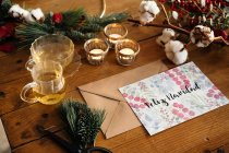 Vista superior da composição de Natal com cartão postal colorido com inscrição Feliz Navidad colocado perto de velas acesas e xícaras de chá em mesa de madeira decorada com galhos coloridos de plantas — Fotografia de Stock