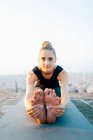 Ganzkörper der flexiblen Frau praktiziert Paschimottanasana auf Sportmatte auf dem Dach bei Sonnenuntergang — Stockfoto