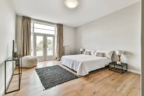 Moderna spaziosa camera da letto arredata con comodo letto con comodino vicino moquette e balcone — Foto stock