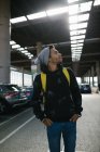 Stylischer afroamerikanischer männlicher Hipster mit Rucksack und Kapuzenpulli steht auf einer Tiefgarage in der Stadt — Stockfoto