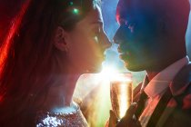 Вид збоку пари культур зі склом на шампанське в момент поцілунку проти блискучого світлого променя, дивлячись один на одного під час вечірки — стокове фото