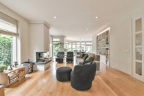 Современный интерьер комнаты с креслами и диваном с декоративными подушками против камина в светлом доме — стоковое фото