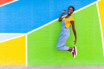 Side view full body of happy African American female smiling while jumping above ground near bright wall — Stock Photo