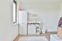 Interior minimalista da sala de luz com roupeiro branco e armário com prateleiras colocadas perto da janela durante o dia — Fotografia de Stock