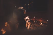 Seitenansicht einer verträumten Zauberin mit gemaltem Gesicht und Totenkopf, die während eines mystischen Rituals in einem Raum mit schummrigem Licht zaubert — Stockfoto