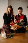 Amigos alegres do sexo feminino em pé à mesa com velas e fazendo buquês de Natal criativos para celebração de férias — Fotografia de Stock