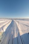 Вид на поезд с беспилотника на железной дороге по заснеженной местности под голубым небом — стоковое фото