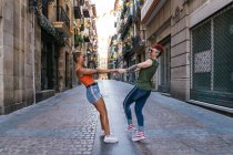 Seitenansicht eines glücklichen jungen homosexuellen weiblichen Paares mit Tätowierungen in trendigen Klamotten, die einander beim Spaß auf der Straße anschauen — Stockfoto