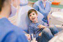 Hoher Winkel des Jungen mit geöffnetem Mund im Gespräch mit Ärzten während der Zahnbehandlung in einer modernen Zahnarztpraxis — Stockfoto