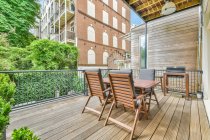 Tavolo in legno e comode poltrone morbide poste sul balcone in legno della casa moderna in campagna in estate — Foto stock