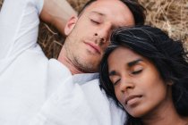 Сверху небритый мужчина с индийской партнершей, спящей на лугу днем — стоковое фото