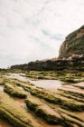 Spectacular view of rough mountain with moss on sandy shore against ocean under cloudy sky in Cantabria Spain — Stock Photo