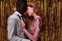 Vista lateral do jovem casal multirracial romântico em vestuário elegante abraçando enquanto celebra a véspera de Ano Novo — Fotografia de Stock