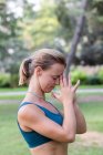 Vista lateral da jovem fêmea em activewear de pé com mãos namaste enquanto pratica ioga no parque verde durante o dia — Fotografia de Stock