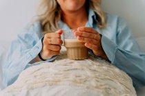 Crop adult female with wavy hair drinking tasty coffee while looking forward in house — Stock Photo