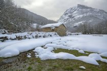 Пейзаж горных склонов и долины покрытые белым снегом с небольшим сельским домом под голубым облачным небом в природном парке Redes, расположенном в Калео-Астуриас, Испания — стоковое фото