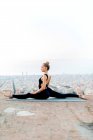 Full body side view of focused barefoot female practicing Hanumanasana position during yoga session on rooftop — Stock Photo