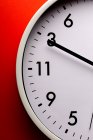 Runde geformte minimalistische Uhr mit Zahlen und Pfeilen auf buntem roten Hintergrund — Stockfoto